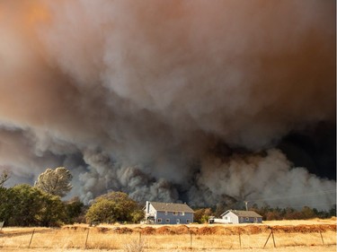 A home is overshadowed by towering smoke plumes as the Camp fire races through town in Paradise, California on November 08, 2018. - More than 18,000 acres have been scorched in a matter of hours burning with it a hospital, a gas station and dozens of homes.