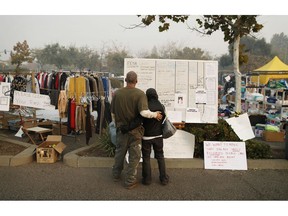 Tera Hickerson, right, and Columbus Holt embrace as they look at a board with information for services at a makeshift encampment outside a Walmart store for people displaced by the Camp Fire, Friday, Nov. 16, 2018, in Chico, Calif. The two, from Paradise, Calif., escaped the fire and don't know if their house is still standing.