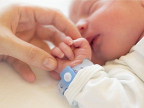 Newborn baby boy sleeping in his crib, his mother's hand holding his little hand. Getty Images/iStockphoto