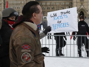 Counter-protesters hold a sign in front of a person attending a rally against the UN international pact on migration, at Parliament Hill in Ottawa, Ontario, on December 8, 2018. - The Global Compact for Safe, Orderly and Regular Migration was finalized at the UN in July after 18 months of negotiations and is to be formally adopted on December 10, 2018, at a conference in Marrakesh, Morocco.