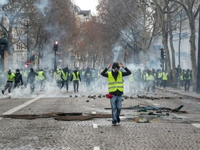 A protestor wearing a "Yellow vest" (gilet jaune) gestures during clash with riot police amid tear gas near the Champs Elysees in Paris on December 8, 2018 during a protest of against rising costs of living they blame on high taxes.