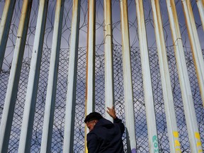 A man holds on to the border wall along the beach, Tuesday, Jan. 8, 2019, in Tijuana, Mexico.