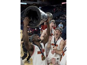 Calgary Dinos' David Kapinga, left, hoists the W.P. McGee trophy while celebrating with teammates after defeating the Ryerson Rams to win the U Sports men's basketball national championship in Halifax on Sunday, March 11, 2018.