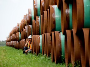 A pipeline worker leans against stockpiled pipe in Alberta.