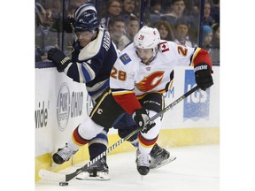 Columbus Blue Jackets' Scott Harrington, left, and Calgary Flames' Elias Lindholm, of Sweden, fight for a loose puck during the third period of an NHL hockey game Tuesday, Dec. 4, 2018, in Columbus, Ohio. The Flames beat the Blue Jackets 9-6.