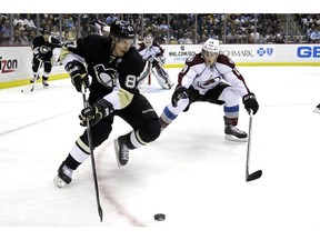 The Pittsburgh Penguins' Sidney Crosby works the puck in the corner against off-season training partner and Colorado Avalanche superstar Nathan MacKinnon. AP file photo.