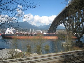 Oil tanker Erik Spirit moves under the Second Narrows Bridge, escorted by a tug (covered by plants in foreground), on March 30, 2019.
