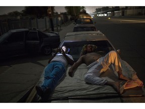 Andres Quintero, left, and Fermin Perez rest on top of Perez's car as they wait in line for over 20 hours to fill their tanks with gas in Cabimas, Venezuela, Thursday, May 16, 2019. U.S. sanctions on oil-rich Venezuela appear to be taking hold, resulting in mile-long lines for fuel in the South American nation's second-largest city, Maracaibo.