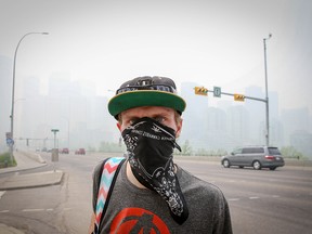 A man wears a bandana over his face as he walks along Centre Street in Calgary on Friday, May 31, 2019. Downtown is barely visible behind him, obscured by smoke from northern Alberta wildfires.