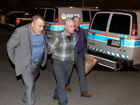 Robert Leeming is brought into arrest processing by detectives of the Calgary Police Service on Monday night. Photo by Mike Drew/Postmedia.