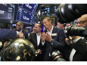 Uber CEO Dara Khosrowshahi center, shakes hands with a trader after his company's initial public offering begins trading at the New York Stock Exchange, Friday, May 10, 2019. He is flanked by Uber's Chief Legal Officer Tony West, left, and board member Ryan Graves, right.