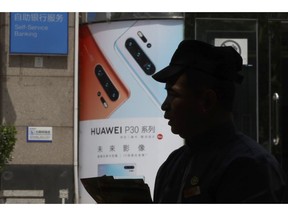 In this photo taken Thursday, May 16, 2019, a man handing out pamphlets is silhouetted against a advertisement for the latest smartphones from Huawei in Beijing. Google is assuring users of Huawei smartphones the American company's services still will work on them following U.S. government restrictions on doing business with the Chinese tech giant.