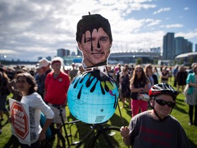 A protester holds a photo of Prime Minister Justin Trudeau and a representation of the globe covered in oil during a protest against the Trans Mountain Pipeline expansion in Vancouver, B.C., on Tuesday May 29, 2018.