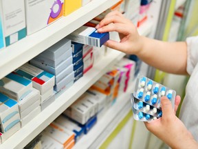 Pharmacist holding medicine box and capsule pack in pharmacy drugstore.