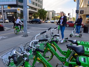 Lime e-scooter riders and cyclist pass by a row of Lime bikes in downtown Calgary on Thursday, Aug. 29, 2019.