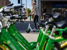 An e-scooter rider passes by a row of Lime bikes in downtown Calgary on Aug. 29, 2019.