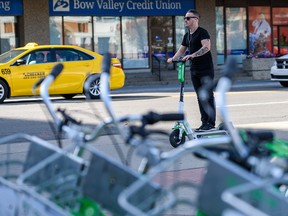 A e-scooter rider passes by a row of Lime bikes in downtown Calgary on Thursday, August 29, 2019.