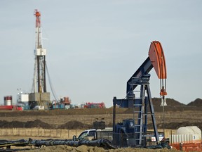 A pumpjack works in the foreground with a drilling rig in the back.