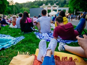 People lay sprawled with their friends on picnic blankets at a park as they watch an outdoor movie.
