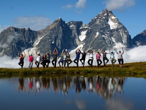 An image of a group of women doing a yoga pose in front of a beautiful mountain scene near Purcell Mountain Lodge in British Columbia.