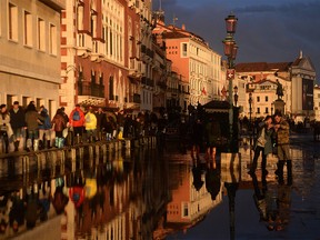 Visitors walk at the sunset in a flooded street in Venice, during "acqua alta", or high water, of 160 centimetres (over five feet), on November 17, 2019. - Venice was braced on November 17 for an unprecedented third major flooding in less than a week, with sea water due to swamp the already devastated historic city where authorities have declared a state of emergency. (Photo by Filippo MONTEFORTE / AFP) (Photo by FILIPPO MONTEFORTE/AFP via Getty Images)