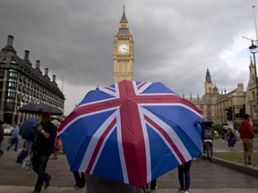 A pedestrian shelters from the rain beneath a Union flag themed umbrella as they walk near the Big Ben clock face and the Elizabeth Tower at the Houses of Parliament in central London on June 25, 2016.