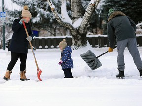 Two year-old Blake Gauthier supervises her parents Mike and Betty as they clear snow from their sidewalk along 6th avenue N.E. after an overnight snowfall on Sunday November 10, 2019.