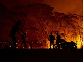 Residents look on as flames burn through bush on Jan. 4, 2020 in Lake Tabourie, Australia.