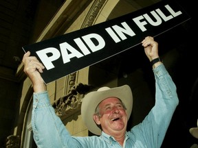 Alberta Premier Ralph Klein holds up a "Paid In Full" sign after announcing in July 2004 that the province's debt of $3.7 billion had been paid off in full ahead of schedule.