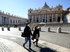 Tourists wearing a protective masks walk in St. Peter's square at the Vatican on February 28, 2020.