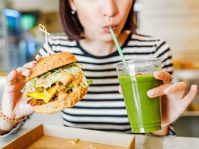 A young woman drinks green smoothies and eats a burger in a vegan fast food restaurant