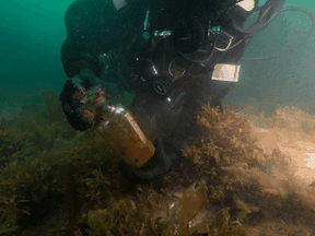 Parks Canada diver Brandy Lockhart picks up a decanter bottle recovered from the HMS Erebus during a dive in August of 2019.
