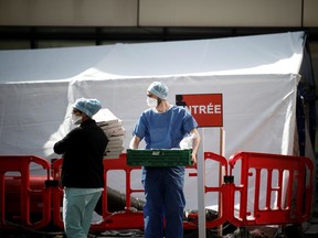 Medical staffs, wearing protective suits, receive prepared foods for caregivers as they stand next to a tent set up for coronavirus disease (COVID-19) patients outside the entrance of the Emergency Department of the Tenon Hospital in Paris as the spread of the coronavirus disease continues in France, March 27, 2020.  REUTERS/Benoit Tessier ORG XMIT: PAR211