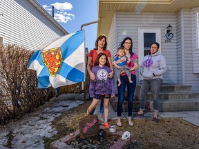 Judy Bastedo, left, and her daughters Emily Rau, holding her 1-year-old son Ben, and Danielle Robertson and her 8-year-old daughter Grace pose for a photo with the Nova Scotian flag waving in the front lawn on Tuesday, April 21, 2020. Azin Ghaffari/Postmedia