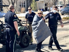 Calgary Fire Dpt and EMS escort a woman to a waiting ambulance in Discovery Ridge in southwest Calgary on  Thursday, April 16, 2020. She had accidentally broken through ice along the Elbow River and was stuck up to her waist in the frigid water and was unable to get out of the cold river by herself. Fire crews arrived and searched the area. The woman remained on the phone with 911 and was then quickly located by firefighters who carefully pulled her out of the water.  She was then transported by a Calgary Fire Department all terrain vehicle to the trailhead and was assessed by waiting EMS. Jim Wells/Postmedia