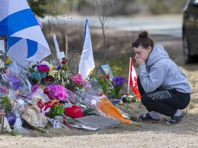 A woman pays her respects at a roadside memorial on Portapique Road in Portapique, N.S. on Friday, April 24, 2020. At least 22 people are dead after a man, who at one point wore a police uniform and drove a mock-up cruiser, went on a murder rampage in Portapique and several other Nova Scotia communities.