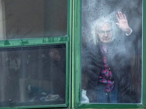 A resident waves from her window on Monday, April 13, 2020, at Residence Herron, a senior's long-term care facility, where there have been a number of COVID-19 deaths.
