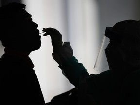 A health worker uses a swab to collect a sample for COVID-19 testing from a man in Gombak on the outskirts of Kuala Lumpur on April 22, 2020.