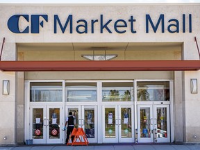 A worker at Market Mall cleans the doors on the north entrance on the shopping centre's first day open after the pandemic on Thursday, May 14, 2020. Many businesses in the mall are still closed and the foot traffic is low.