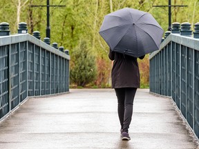 A woman is walking towards the Prince's Island Park holding an umbrella on a rainy morning on Tuesday, May 19, 2020.