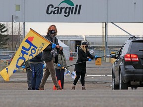 UFCW Local 401 president Thomas Hesse holds flags as other union members used poles to hand out masks and information to workers entering the Cargill plant near High River on Monday, May 4, 2020.