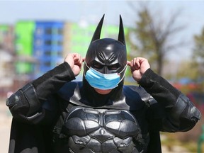 The character Holybatman puts on a surgical mask as he makes a visit outside the Children's Hospital in Calgary on Friday, May 15, 2020. He said it was his first time out in the warmer weather.