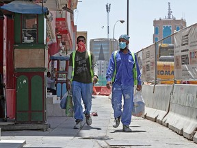 Workers wearing protective masks walk by on a street in Qatar's capital Doha, on May 17, 2020, as the country begins enforcing the world's toughest penalties for failing to wear masks in public, as it battles one of the world's highest coronavirus infection rates.