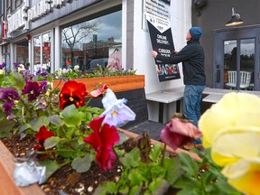 Some spring flowers frame a worker at MARKET restaurant on 17th Avenue in Calgary as he adds a sign advertising the establishment's delivery and pickup offerings on Tuesday, May 12, 2020.