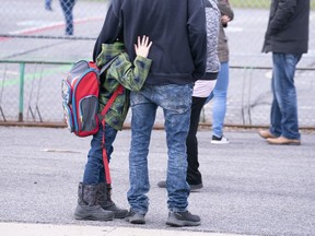A boy hugs his father as he waits to be called to enter the schoolyard the Marie-Derome School in Saint-Jean-sur-Richelieu, Que. on Monday, May 11, 2020. Quebec's education department says a total of 41 students and teachers have tested positive for COVID-19 since primary schools outside the Montreal area opened on May 11.
