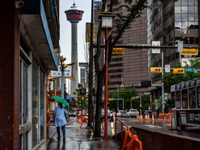 A pedestrian takes shelter under an umbrella as a fleeting rain falls in Chinatown in Calgary on Wednesday, June 24, 2020.