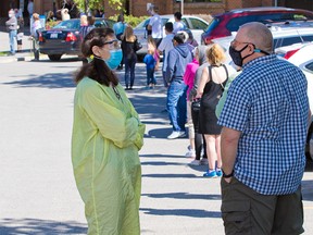 A nurse talks with Calgarians lining up for the new drop-in COVID-19 testing clinic a the Richmond Road Diagnostic and Treatment Centre on Wednesday, June 3, 2020.