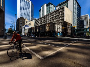 A cyclist crosses an intersection in downtown Calgary, with reflected light from the Husky buildings creating patterns on the pavement on Wednesday, June 10, 2020.