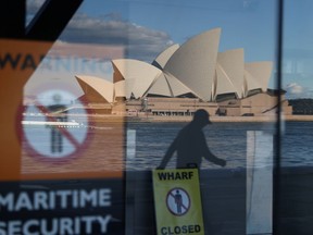 A man, seen reflected in a window, walks in front of the Sydney Opera House following the easing of restrictions implemented to curb the spread of the coronavirus disease (COVID-19) in Sydney, Australia, June 23, 2020.