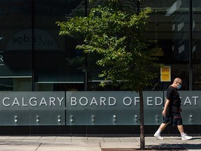 A pedestrian and his dog walk in front of the Calgary Board of Education headquarters on Tuesday, August 4, 2020.